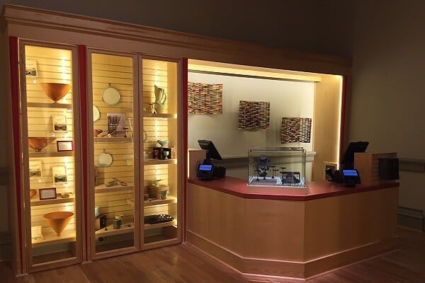 A point of sale station with two registers. Front of station is wood panelled. Behind the station are glass display cases with art for sale.